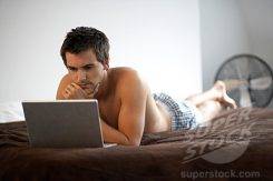Young man with a laptop, laying on a bed